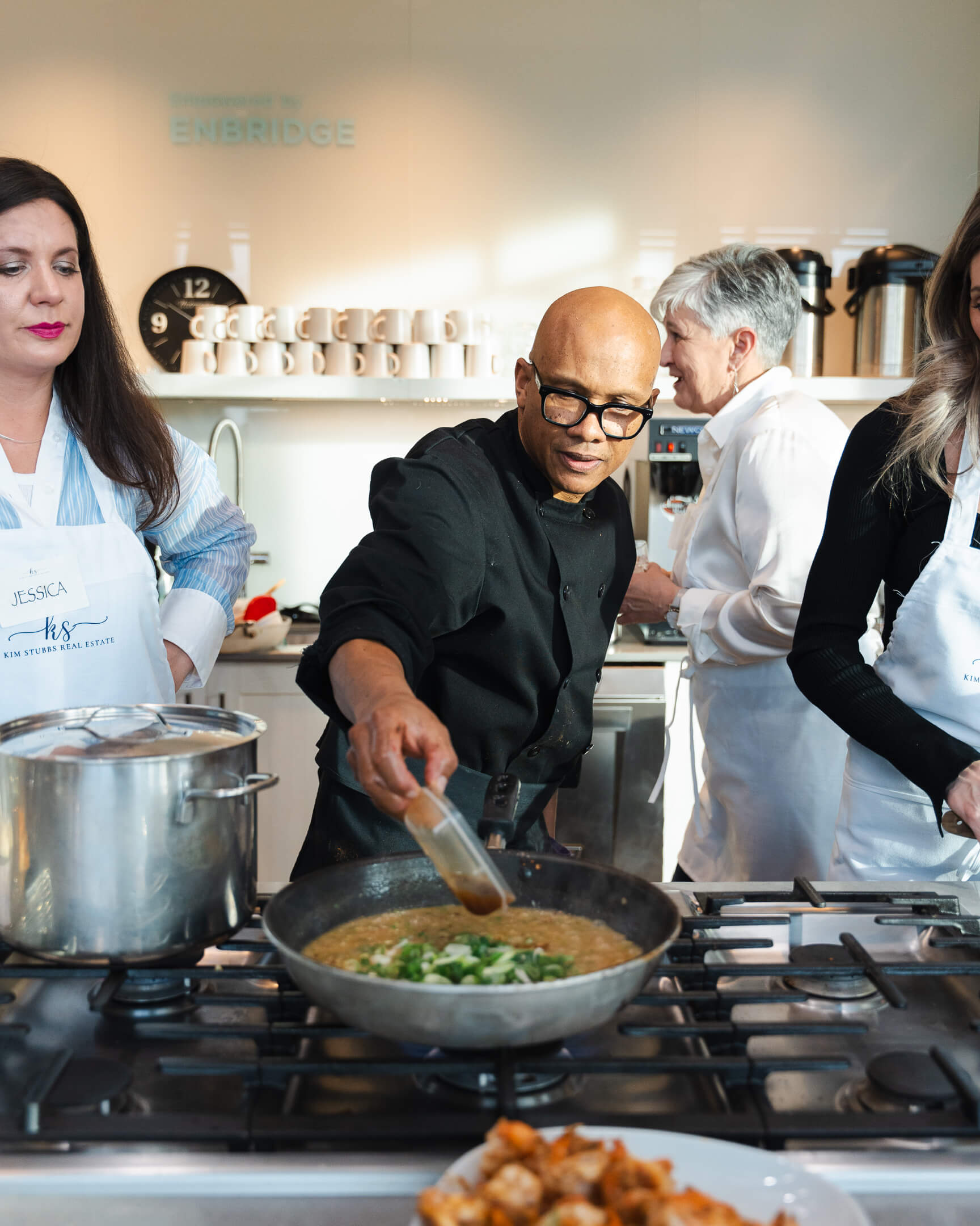 Chef Joey stirring a pan at the stove while participants watch during a hands-on cooking class