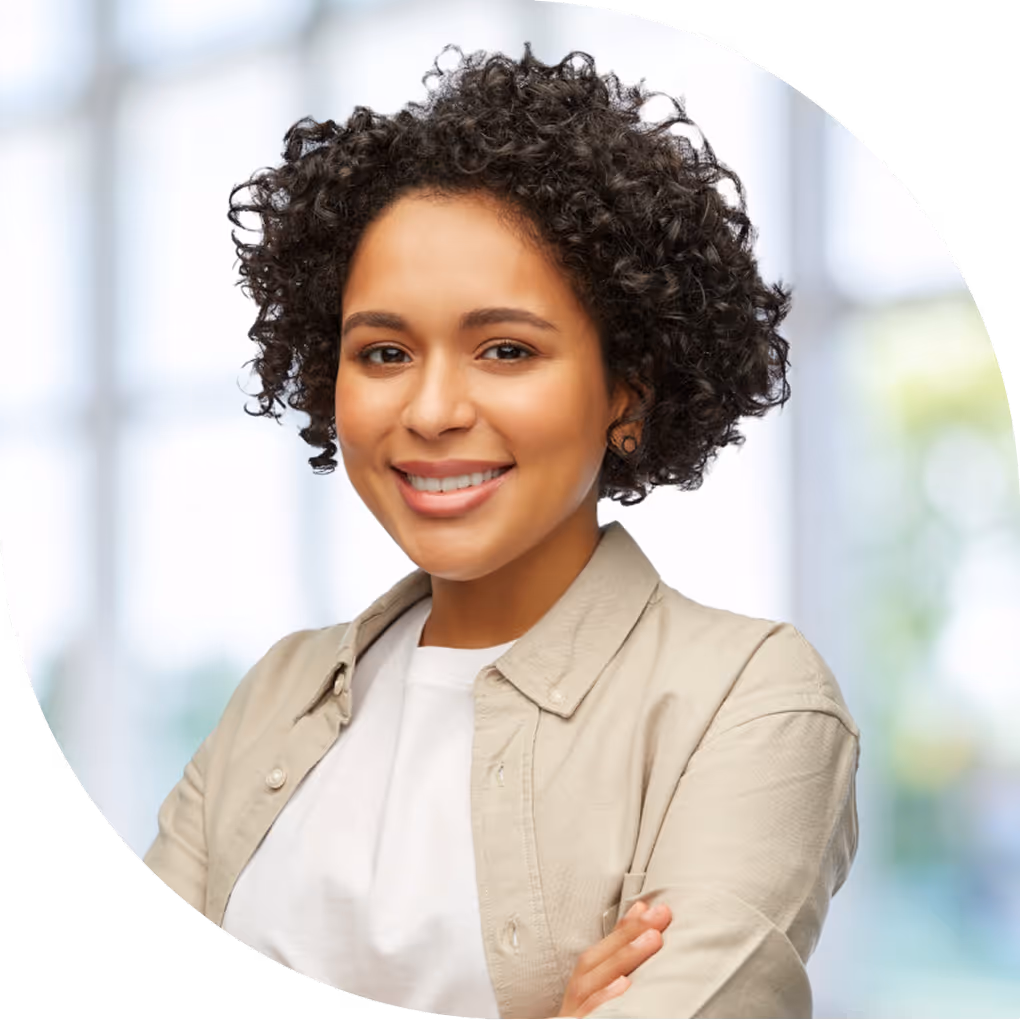 Smiling woman with curly hair wearing a beige jacket and white shirt with arms crossed.