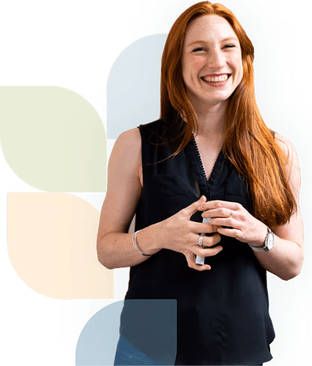 Smiling woman with long red hair wearing a sleeveless black top holding a white object.