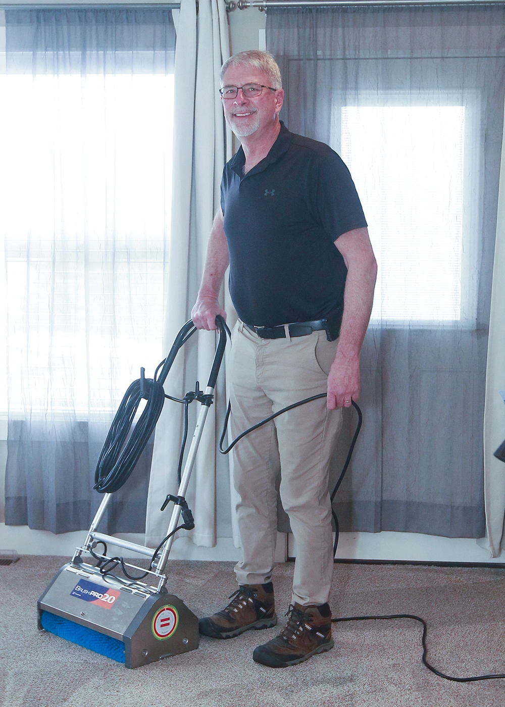 Dean in glasses and black shirt standing on carpet holding a carpet cleaning machine.