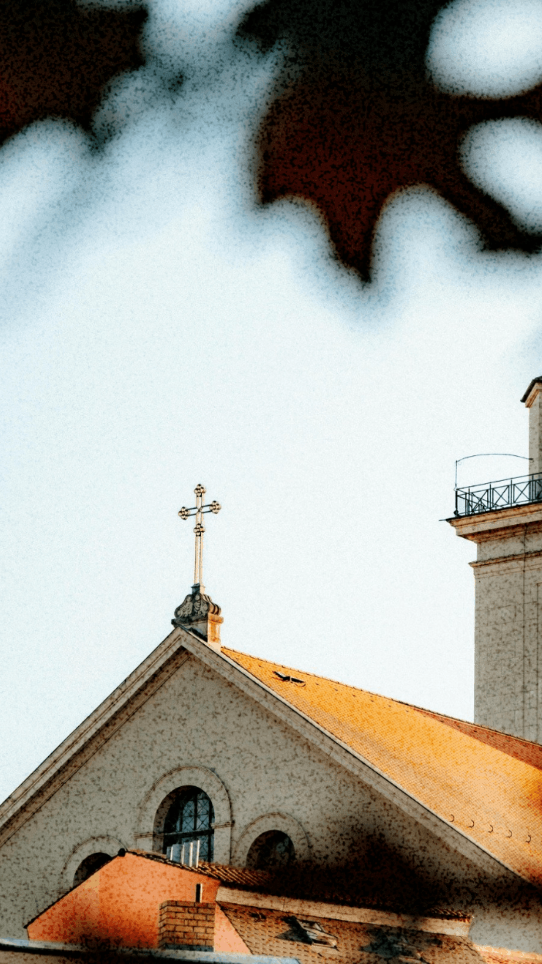 Church roof with a golden cross atop its triangular facade under a partly cloudy sky.