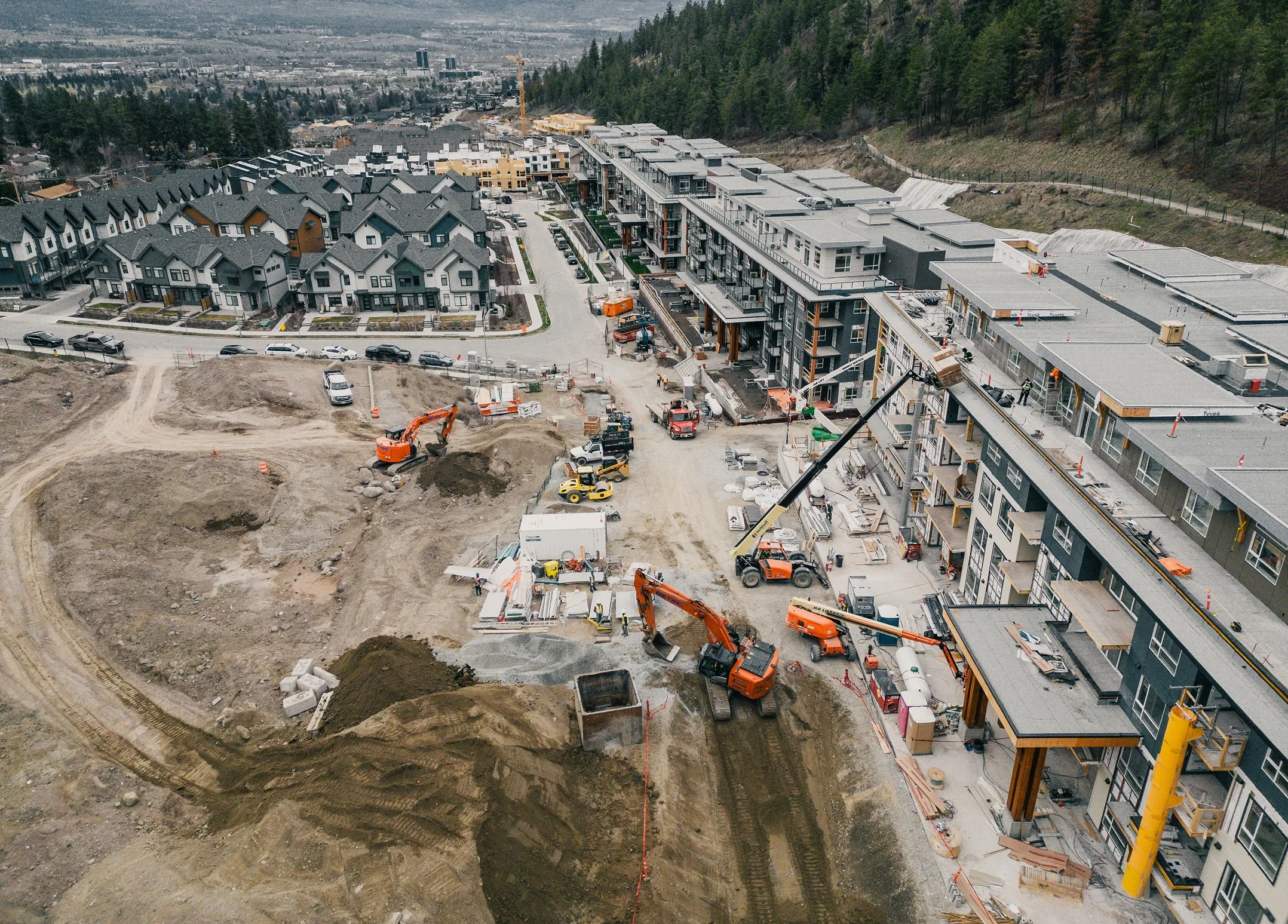 Aerial view of a residential construction site with machinery, new houses, and a large apartment building.