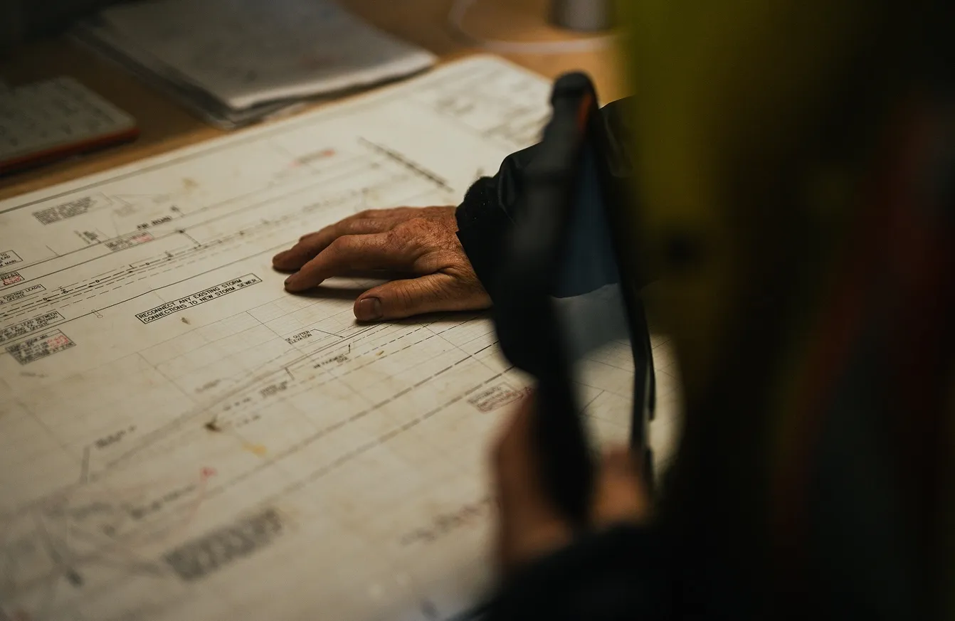 Hand resting on a technical blueprint with construction plans and annotations.