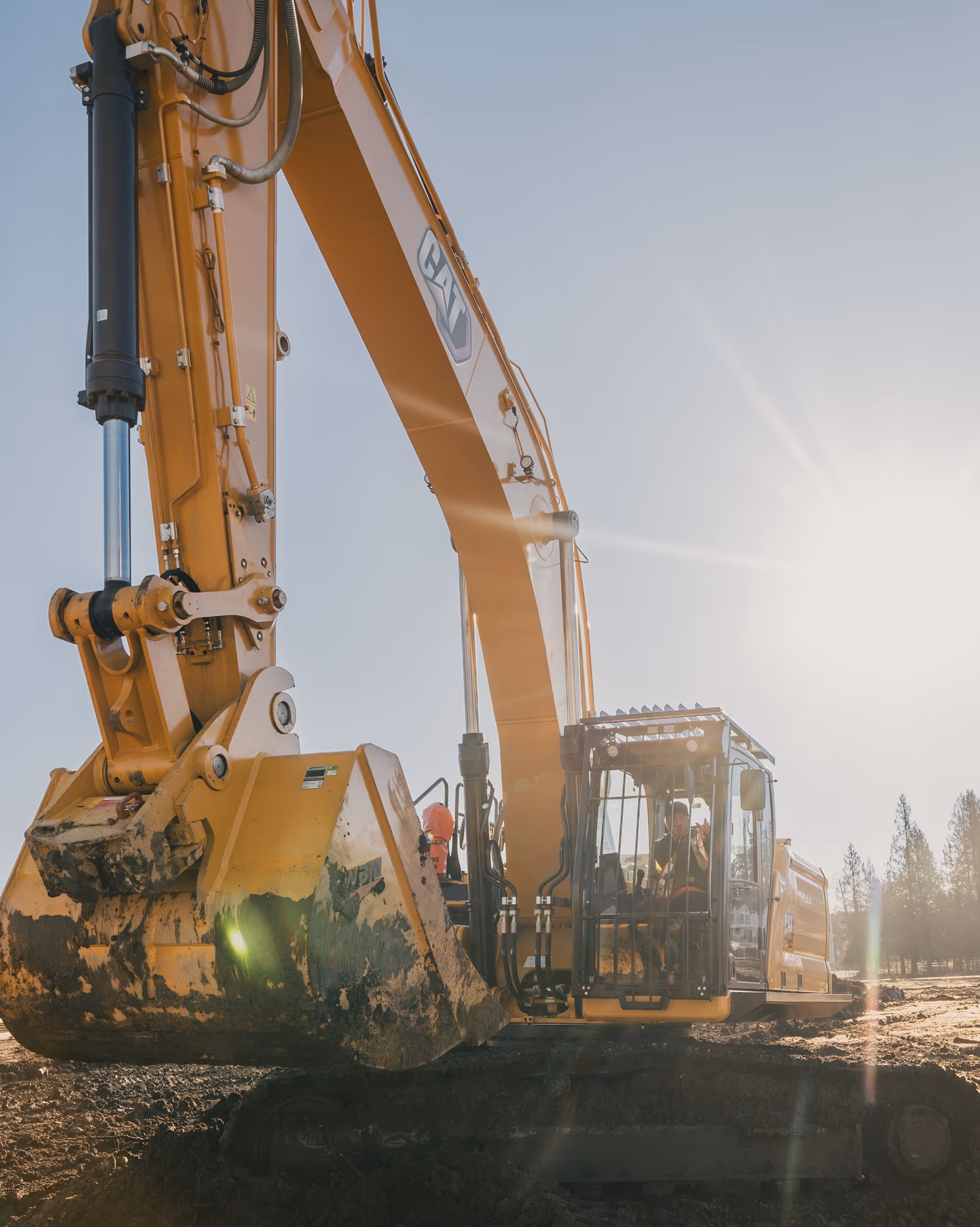 Yellow hydraulic excavator with mud on bucket working on construction site at sunrise or sunset.