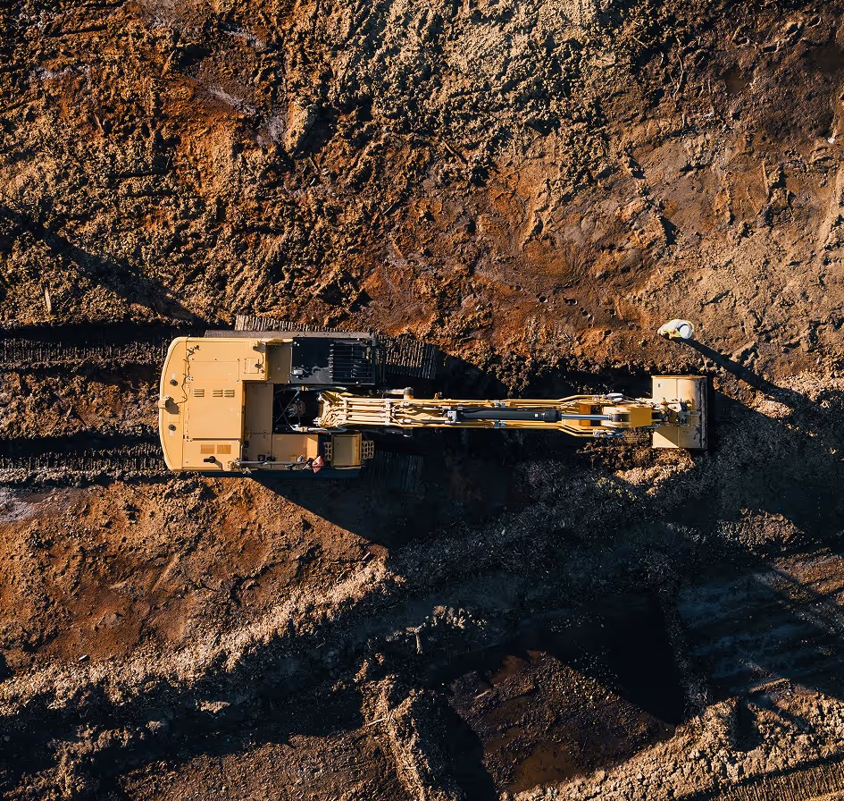 Aerial view of a yellow excavator digging in brown soil on a construction site.