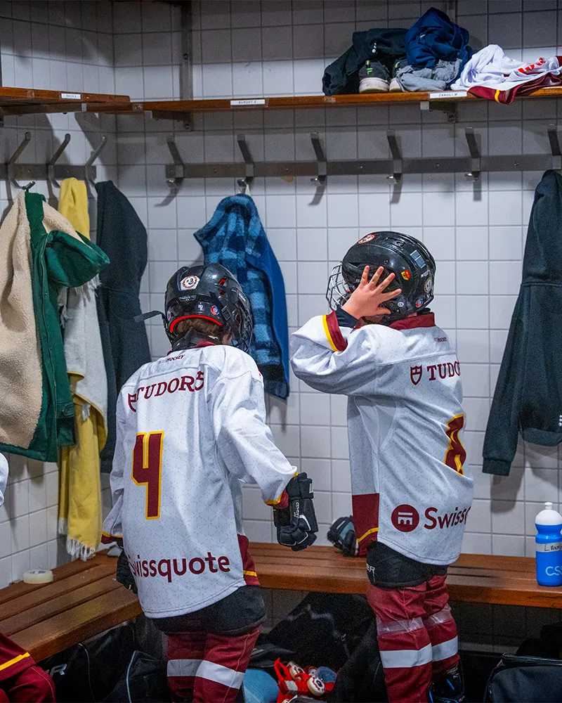 Deux jeunes joueurs de hockey en tenue dans un vestiaire, préparant leur casque.