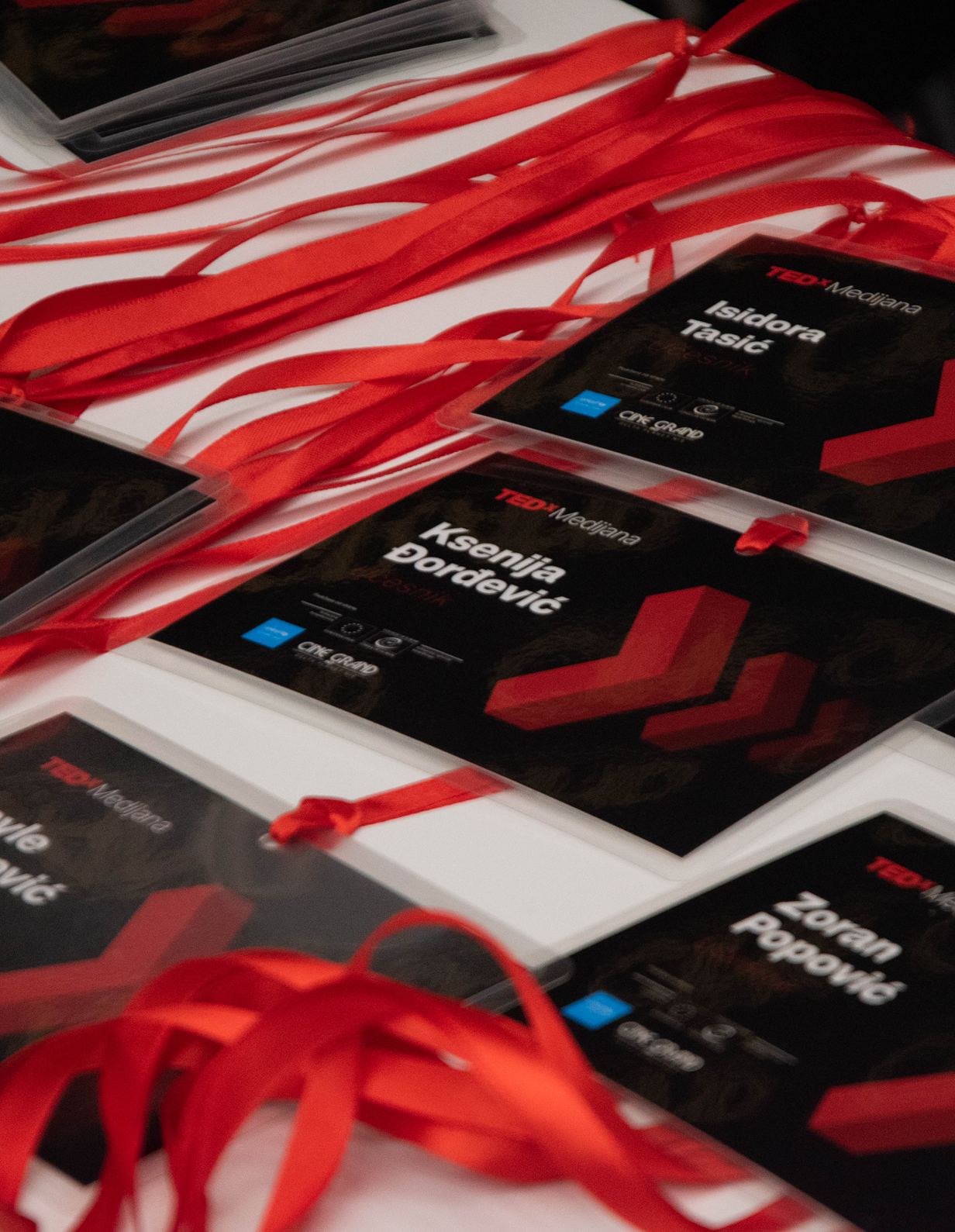 Identifikacione bedževe sa crvenim trakama za TEDx događaj na stolu.