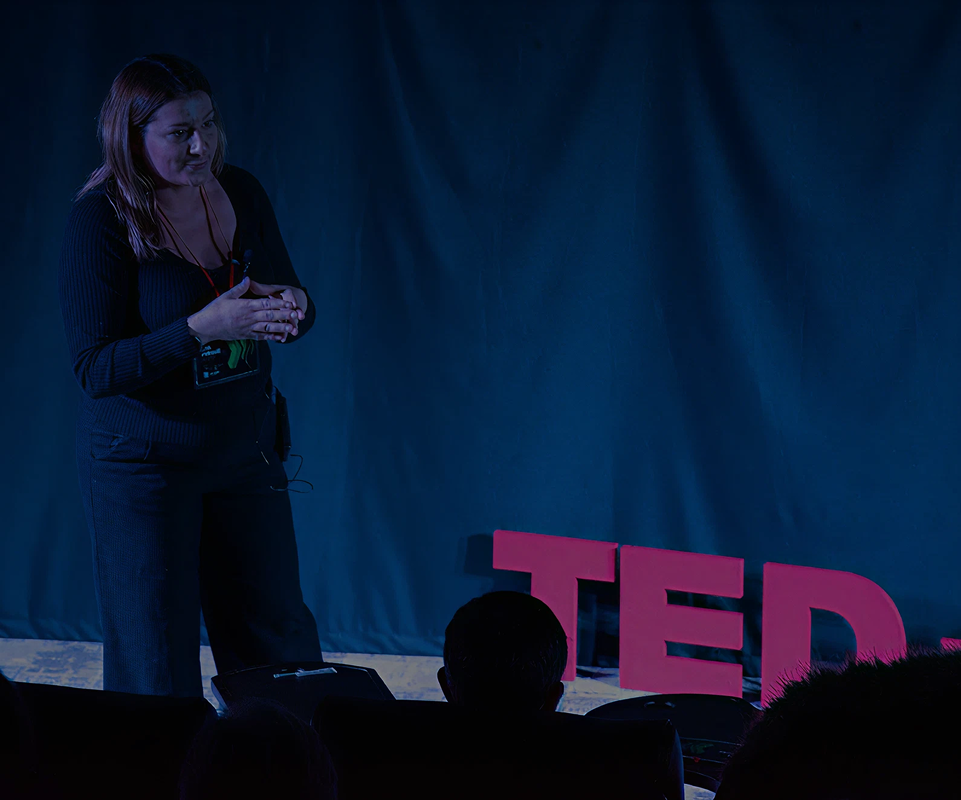 Žena drži govor na pozornici sa velikim crvenim slovima TED u pozadini.