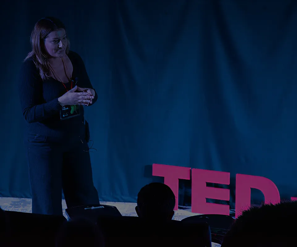 Žena drži govor na pozornici sa velikim crvenim slovima TED u pozadini.