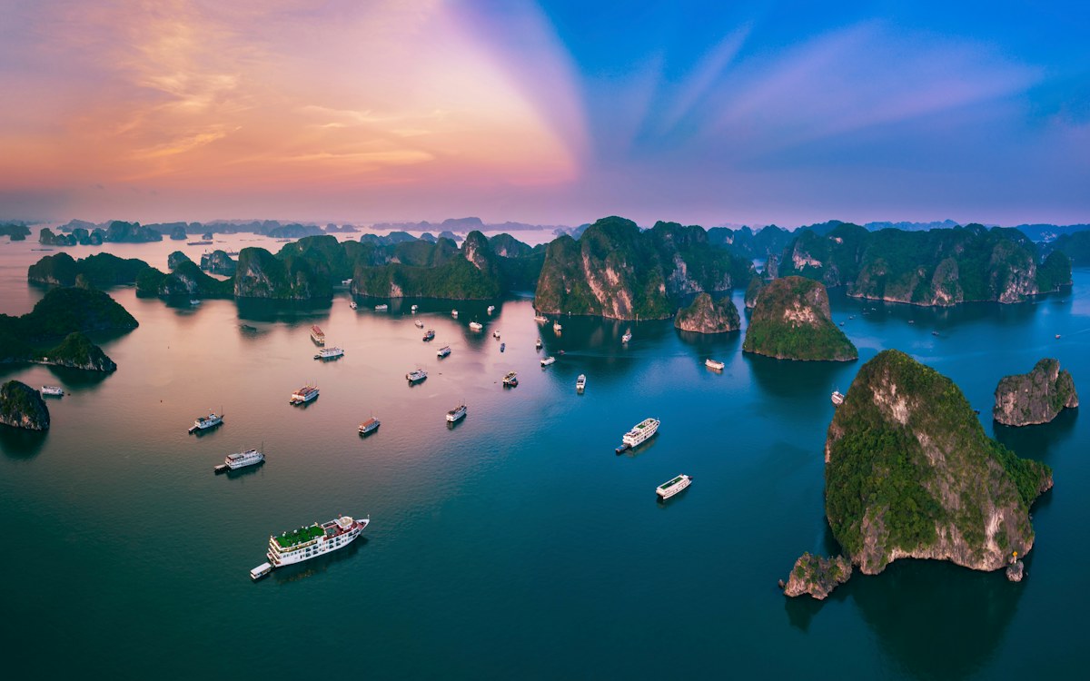 Limestone karst islands and cruise boats in Ha Long Bay, Vietnam, at sunset