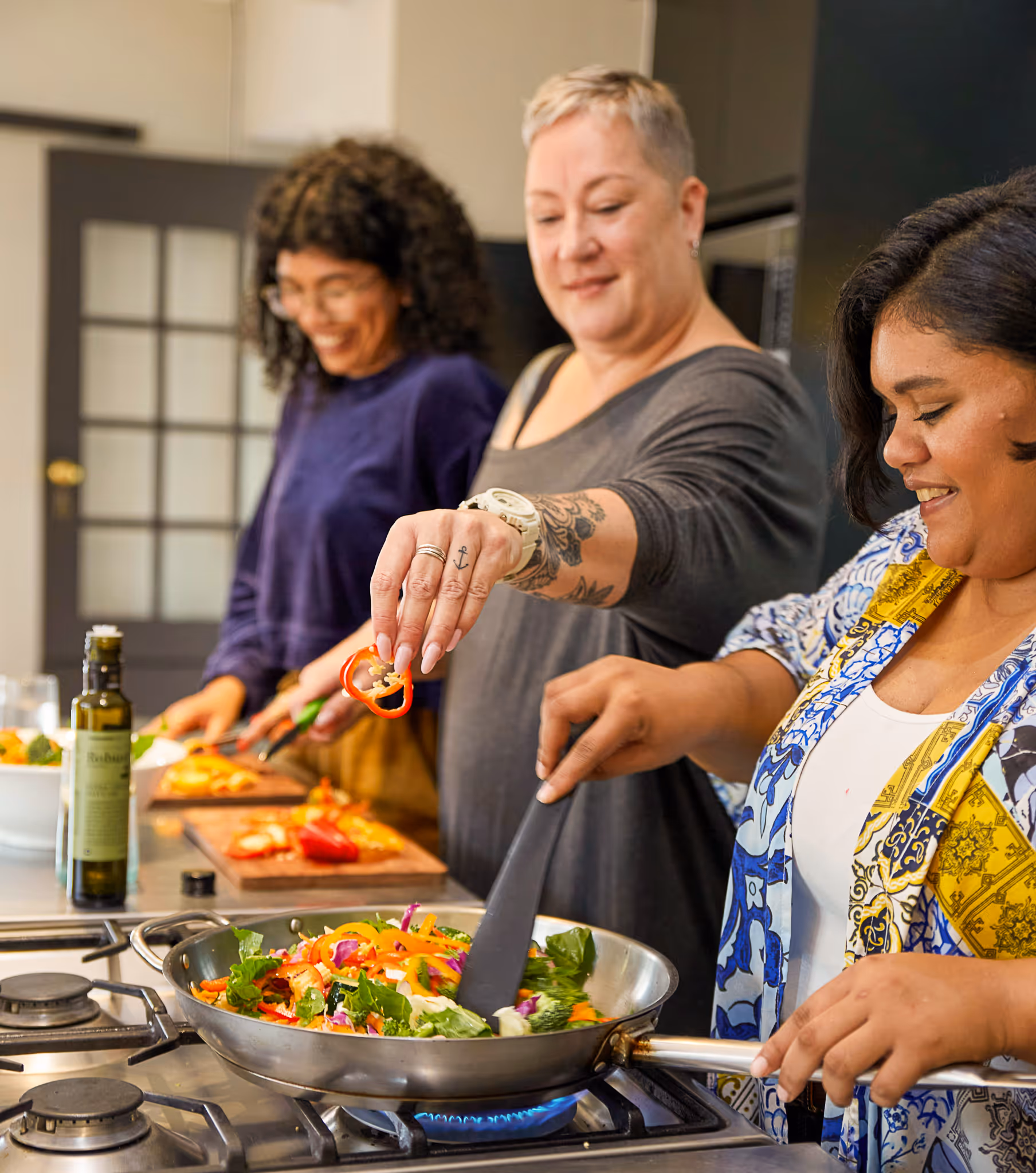 Three women of different generations cooking and preparing vegetables together in a home kitchen