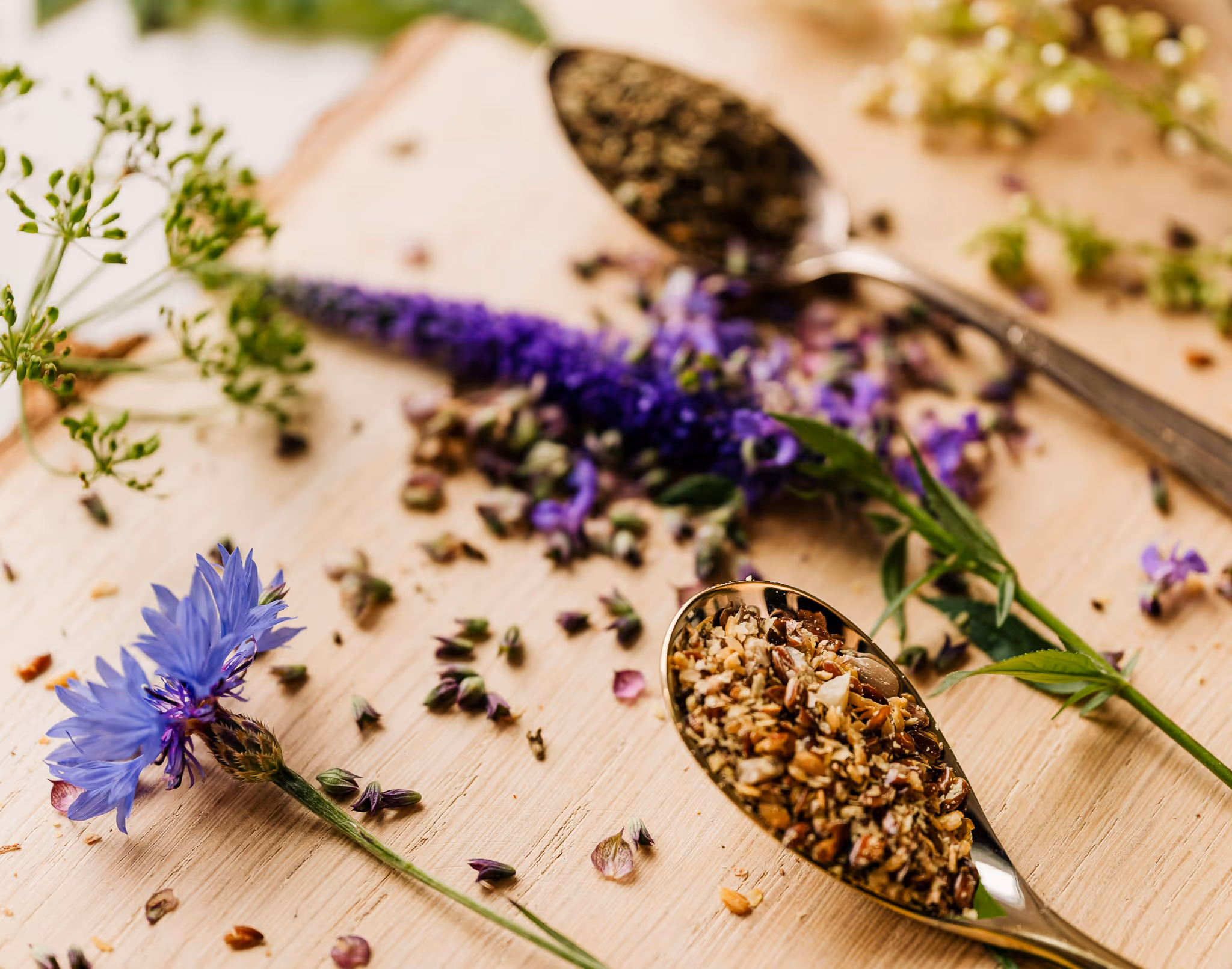 Flat lay of wildflowers, scattered seeds, and a small wooden spoon on a cream surface