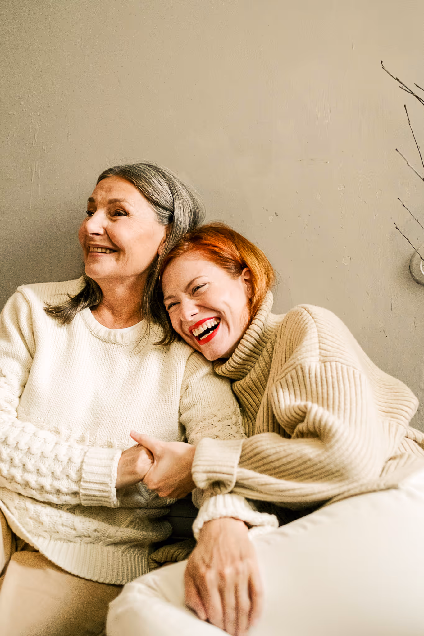 Two women in soft cream clothing embracing and laughing together warmly