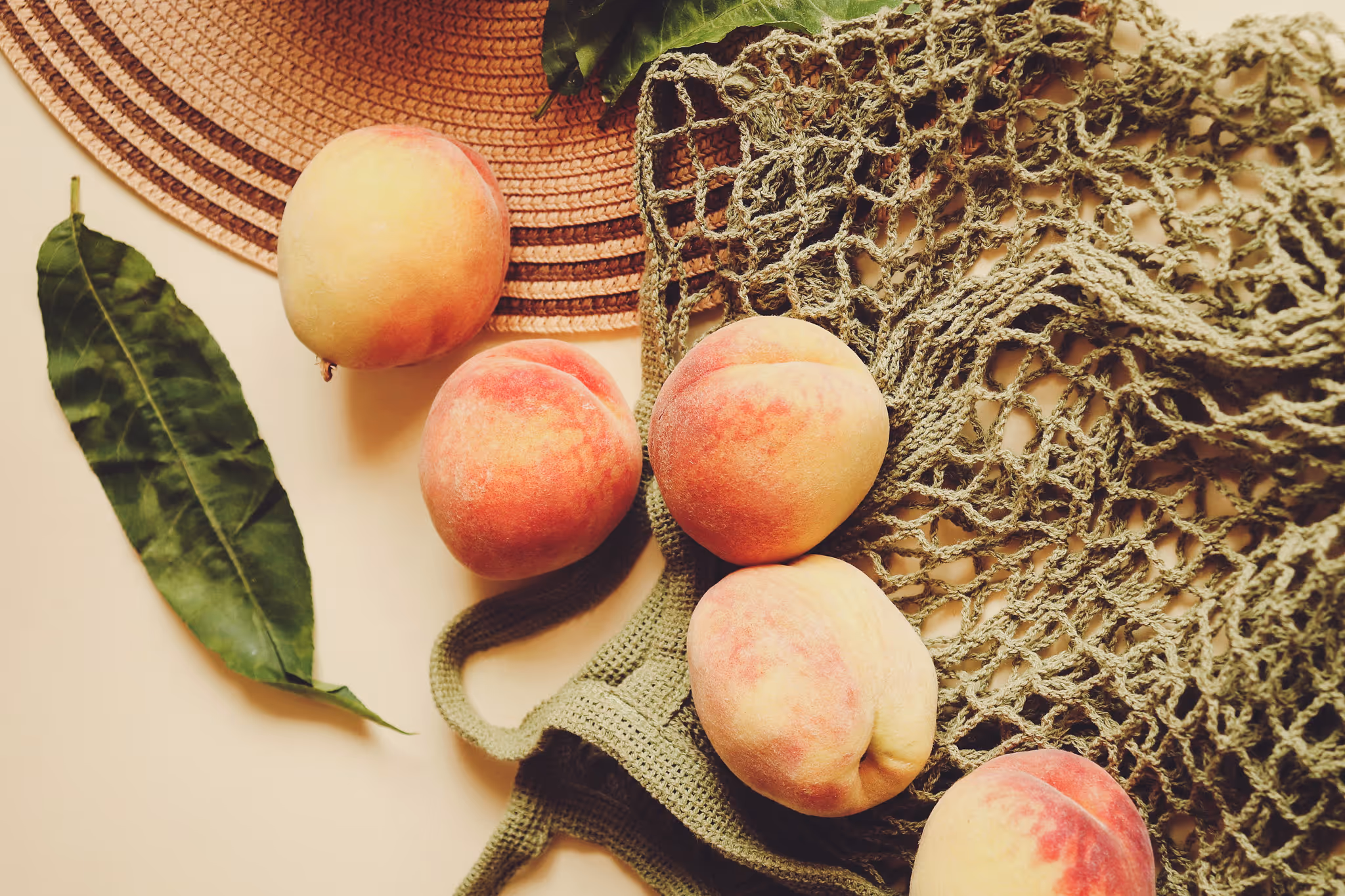 Still life of fresh peach halves, dried botanical sprigs, and a wooden cutting board on a neutral background