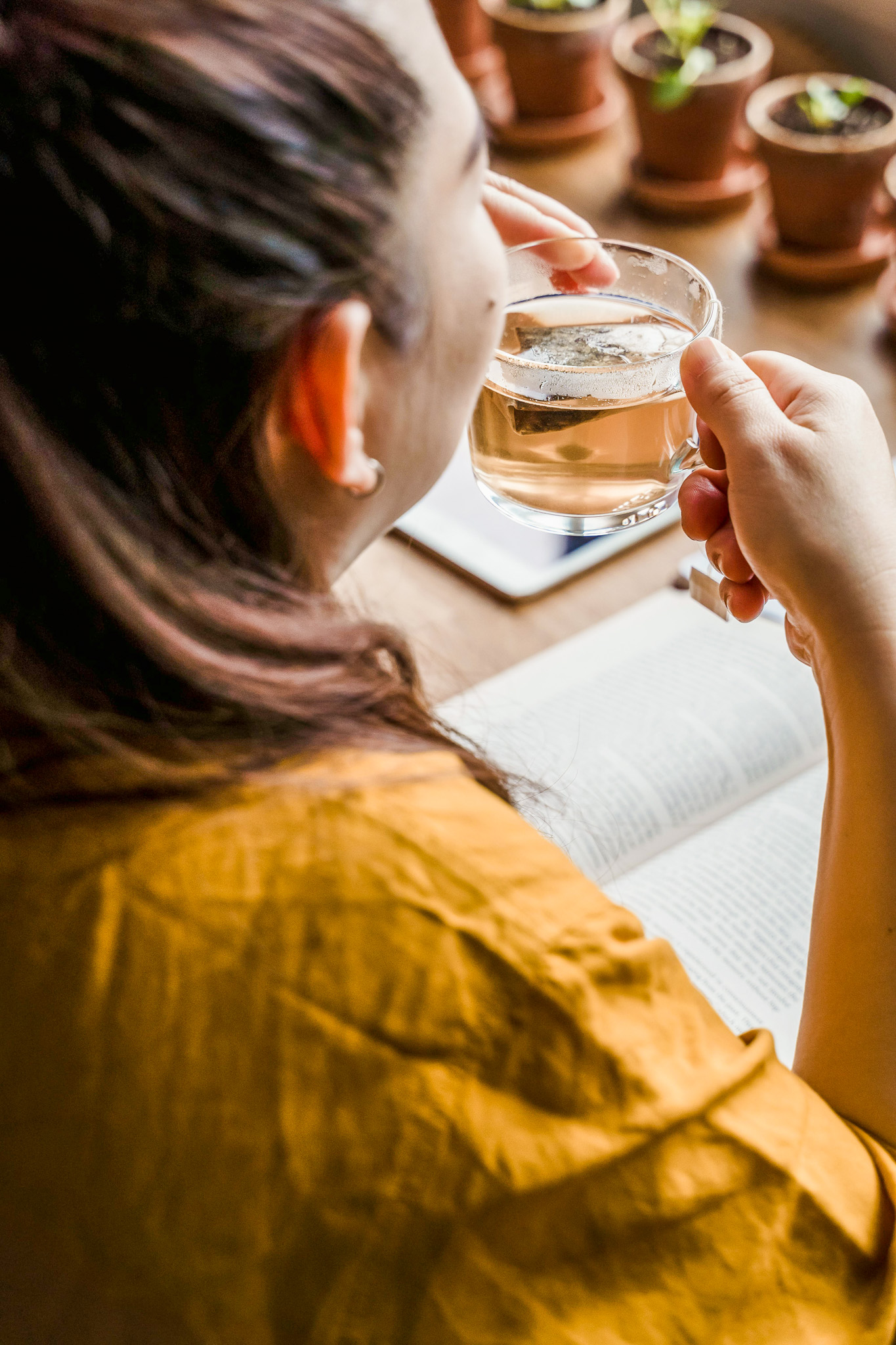 A woman facing away from the camera looking out the window drinking tea and journaling