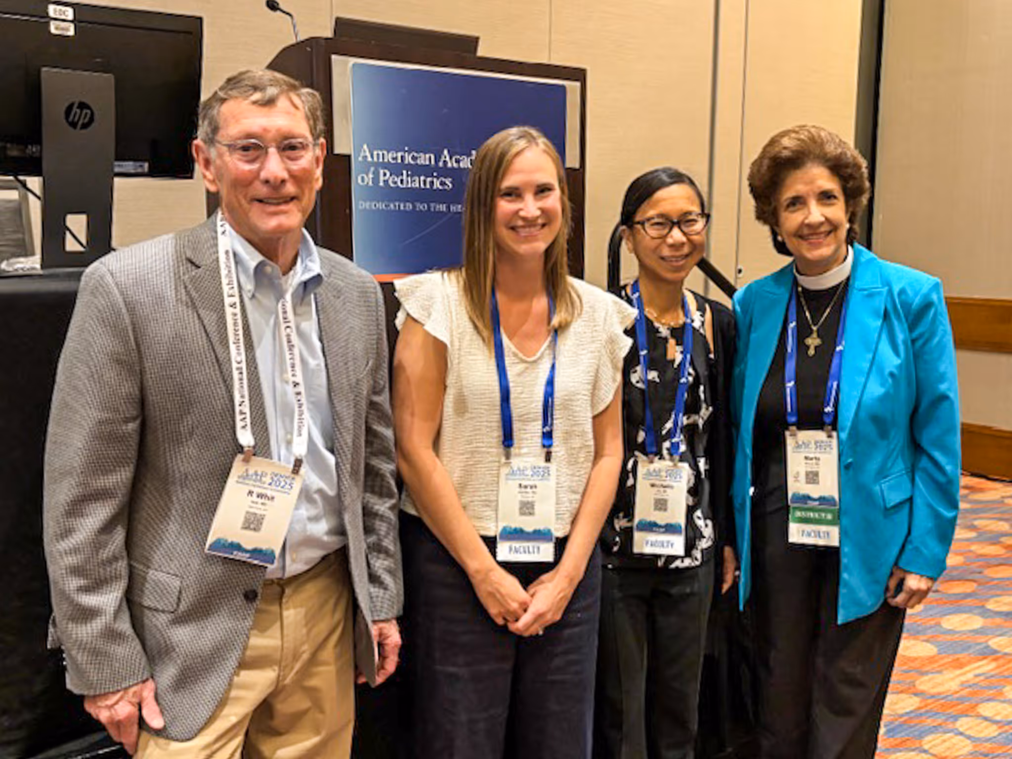 Four faculty members including Dr. Loy posing in front of an American Academy of Pediatrics sign at a conference.