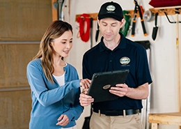 Worker in uniform explaining a tablet screen to a smiling woman in a workshop.