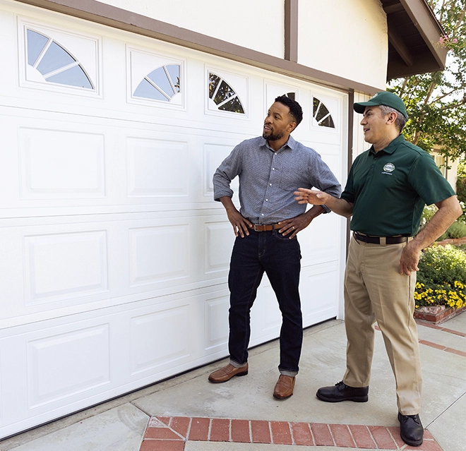 Worker in uniform explaining features of a white garage door to a man in casual clothes.