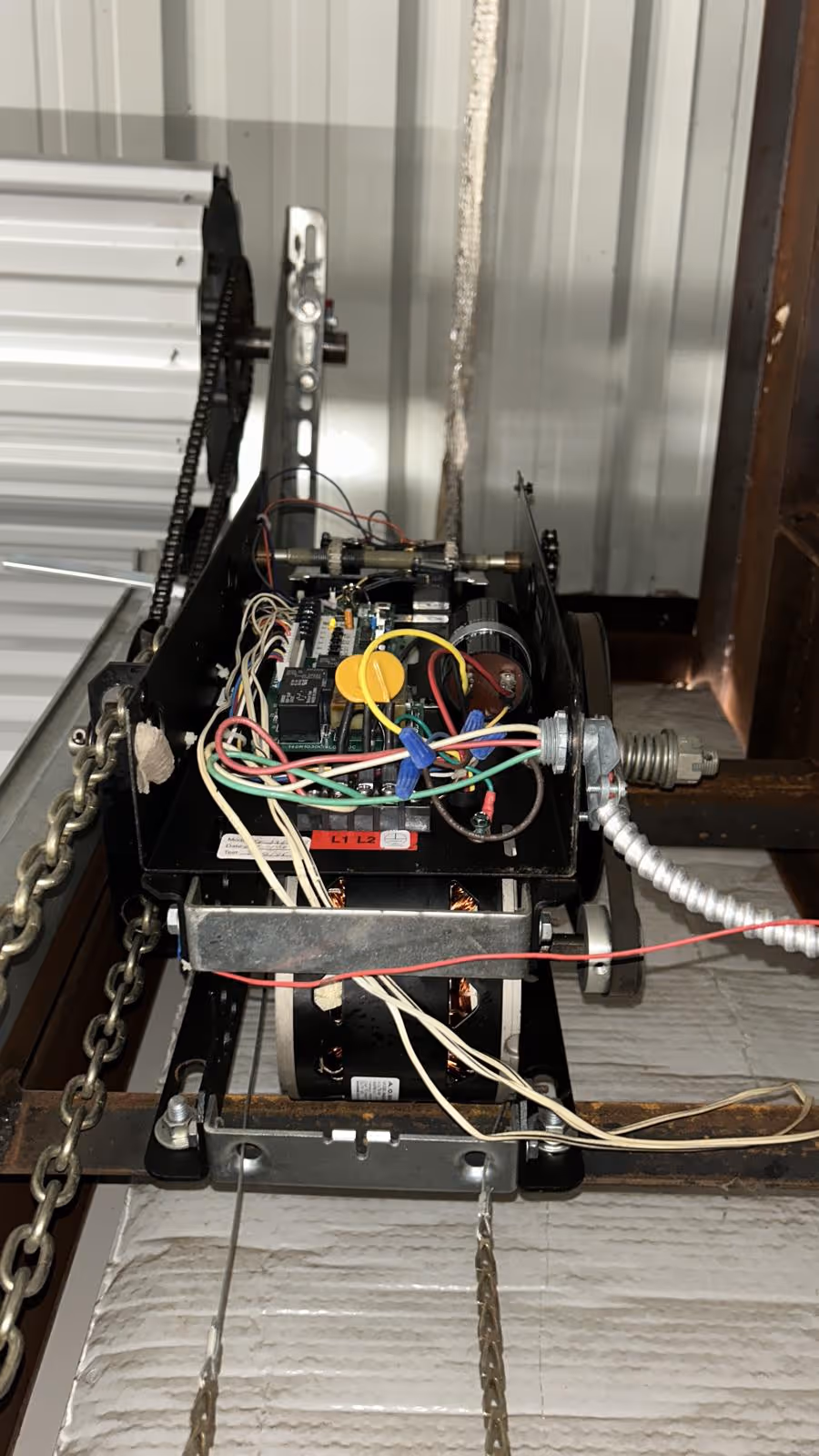 Internal components of an automatic garage door opener including circuit board, motor, chains, and wiring.