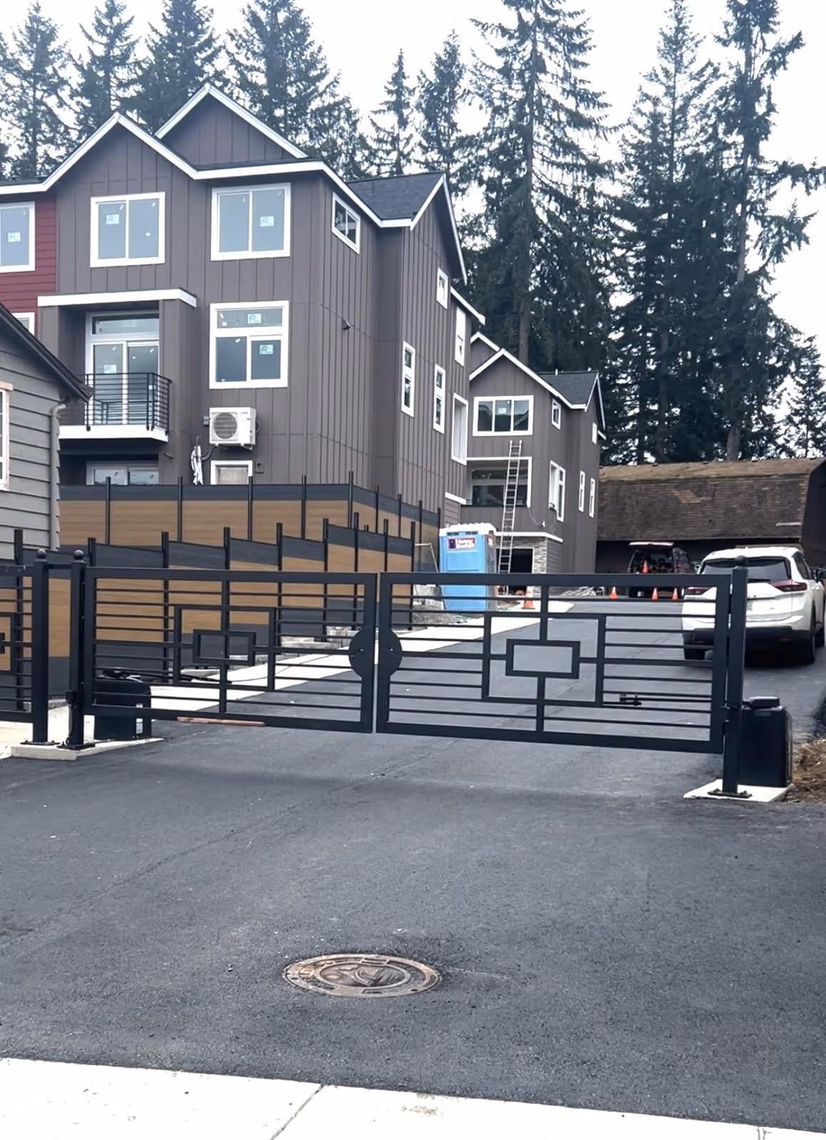 Modern gated entrance with geometric black metal gate in front of multi-story residential buildings.