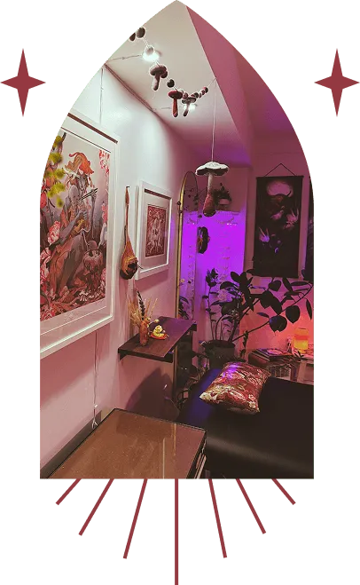 Cozy indoor corner with framed artwork, hanging mushroom decorations, a leafy plant, and a couch with a patterned pillow under warm ambient lighting.