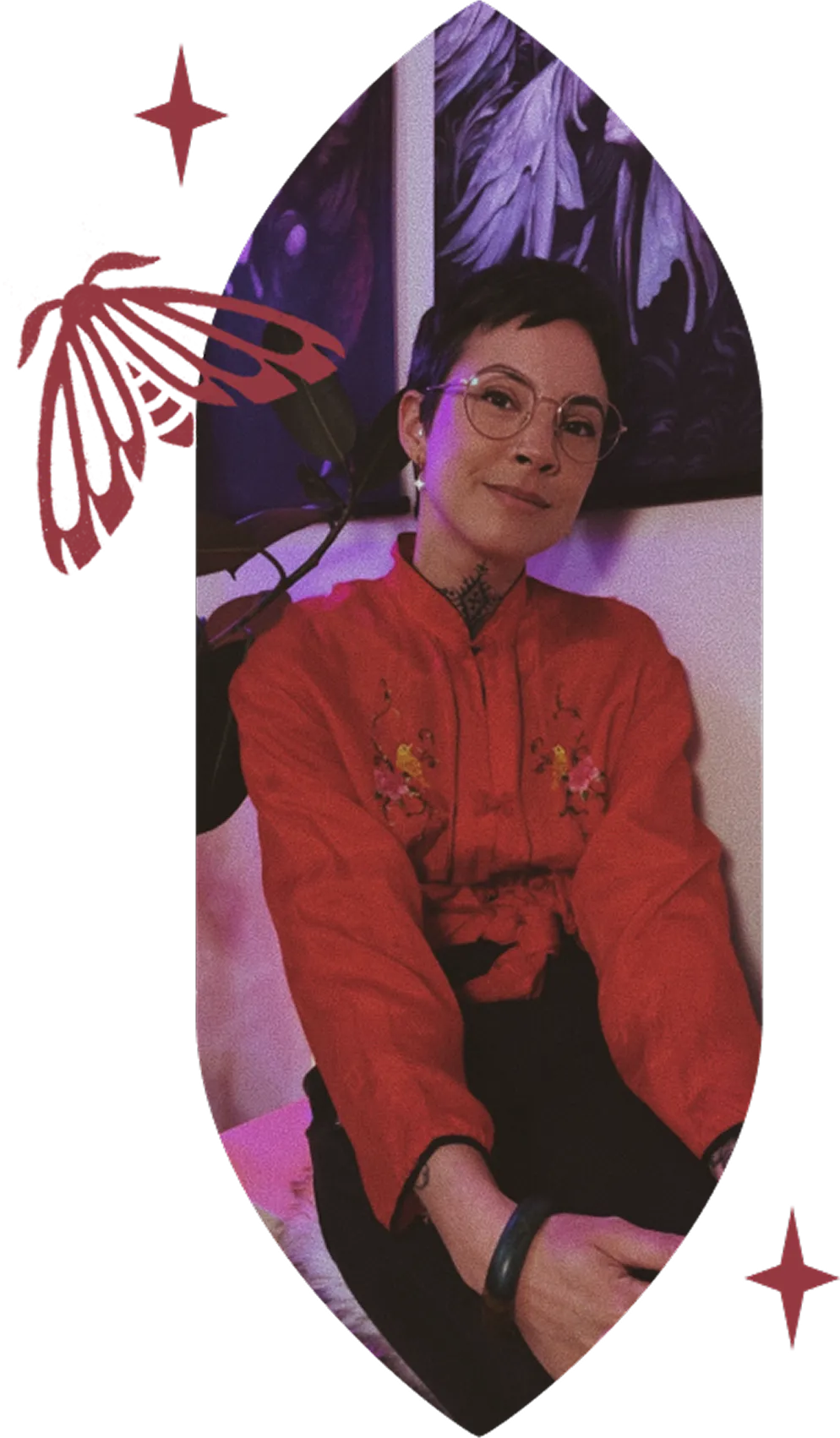 Alyssa, owner of Vale of the Fae wearing a red embroidered jacket, sitting and smiling slightly, with purple artwork in the background.