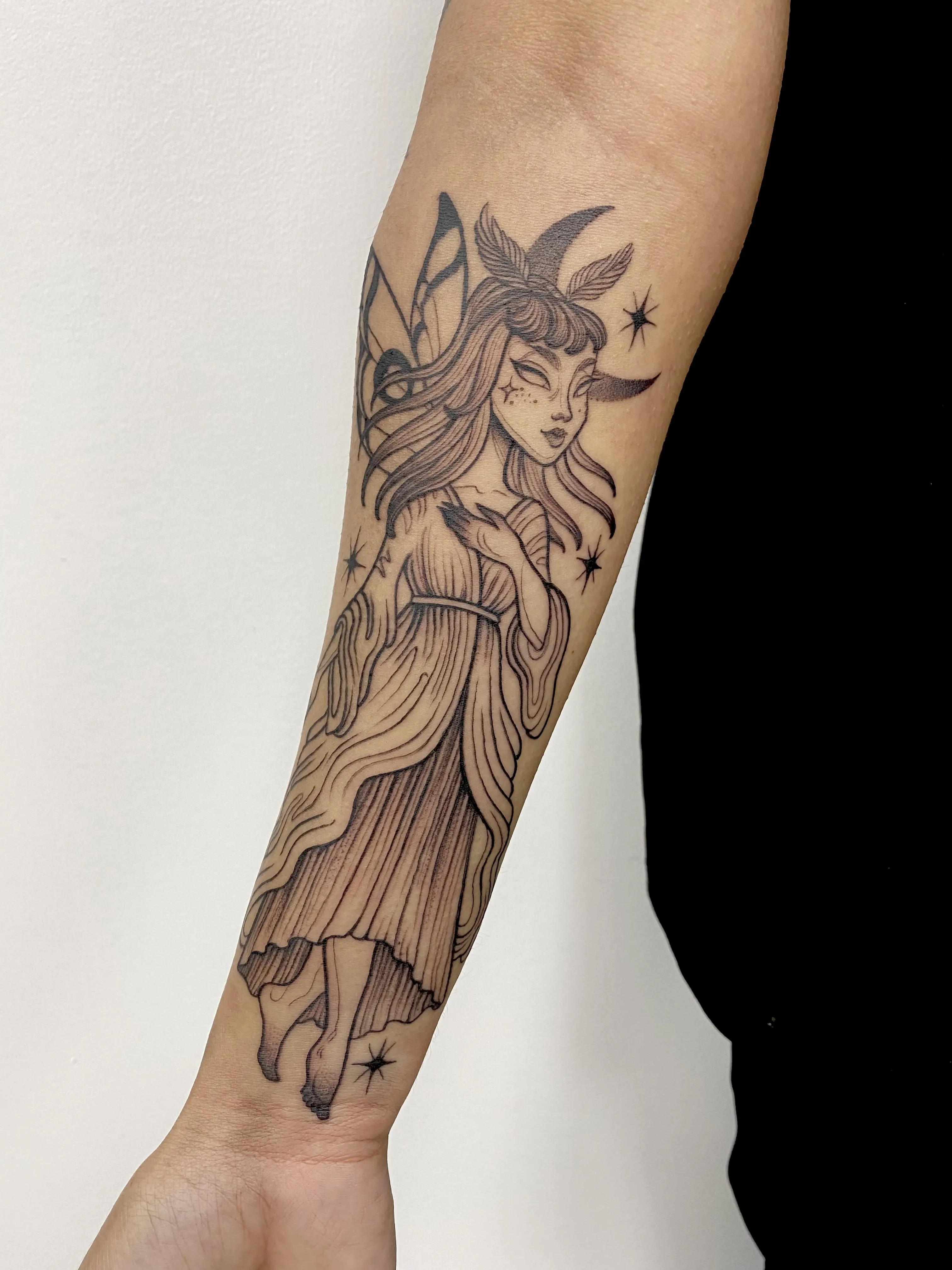 Blackwork forearm tattoo of a winged nymph with flowing hair, a crescent moon and stars, by Alyssa at Vale of the Fae in Castlegar, BC