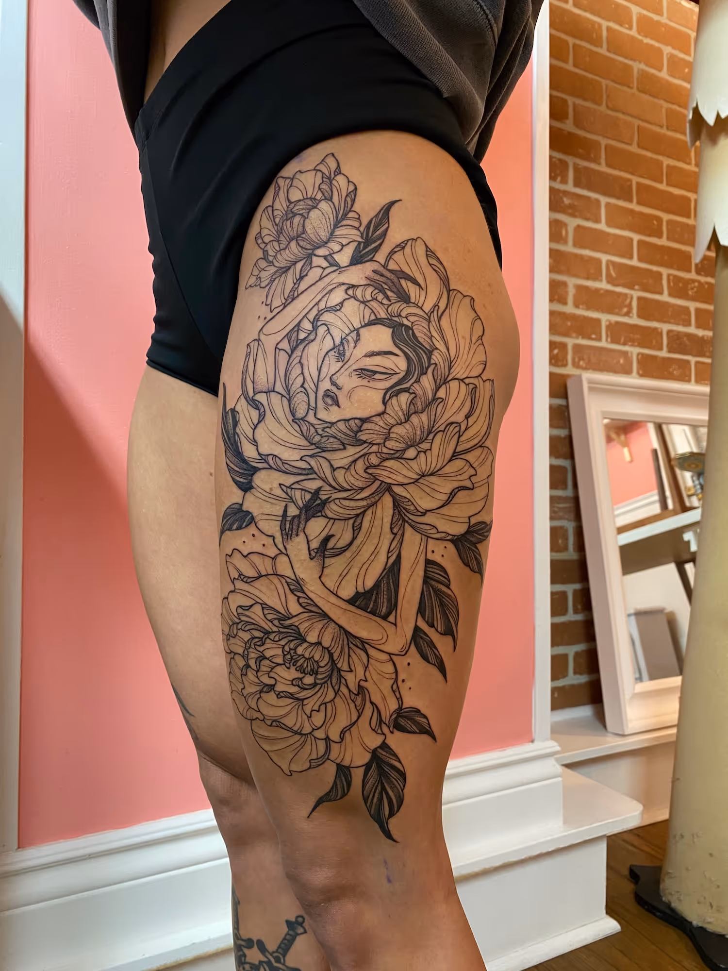 Blackwork thigh tattoo of a stylized goddess surrounded by large flowers, by Alyssa at Vale of the Fae in Castlegar, BC