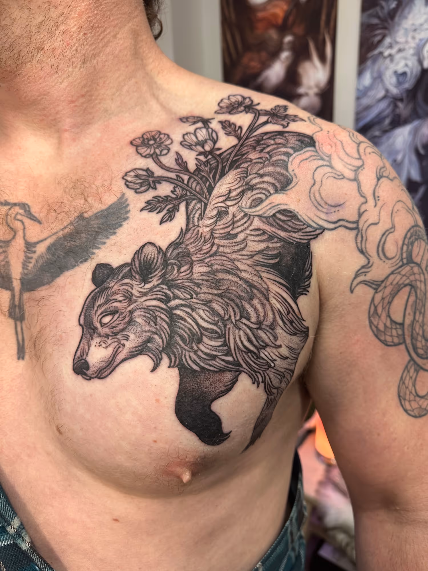 Black and grey bear tattoo with flowers growing from its back on the chest and shoulder, by Alyssa at Vale of the Fae in Castlegar, BC