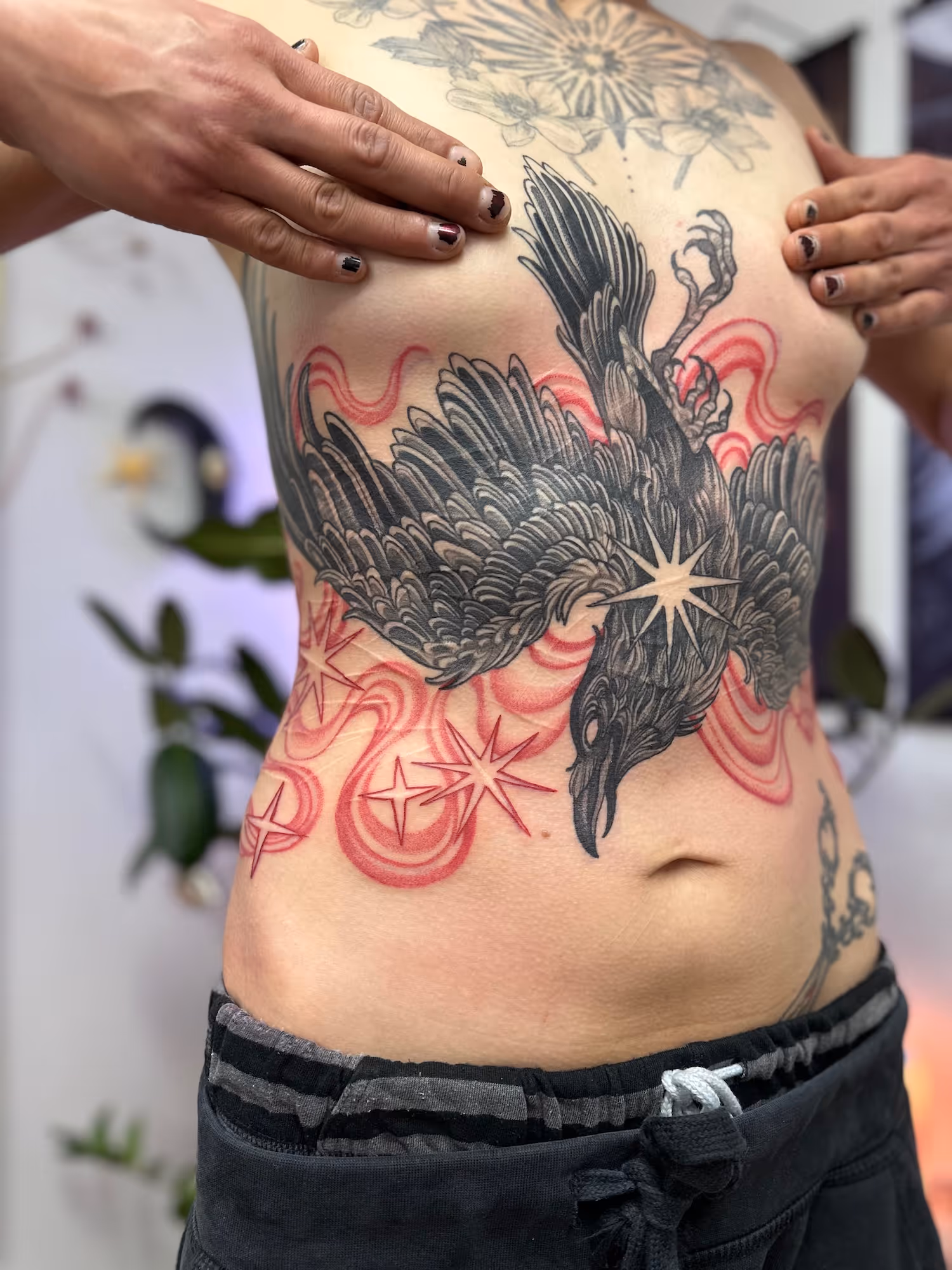 Blackwork raven tattoo with detailed feathers and red stars across the stomach and ribs, by Alyssa at Vale of the Fae in Castlegar, BC