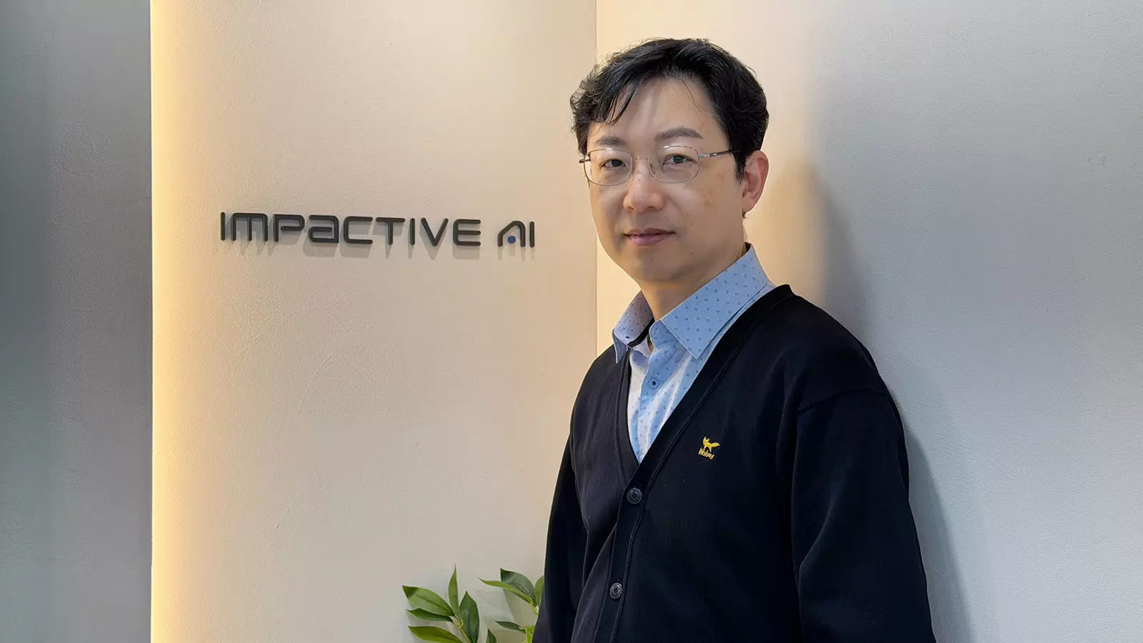 사무실 벽면에 설치된 임팩티브AI 로고 앞에서 정장을 입은 남성이 서 있는 모습, AI 기반 ERP 및 SCM 솔루션을 제공하는 기업 분위기 연출