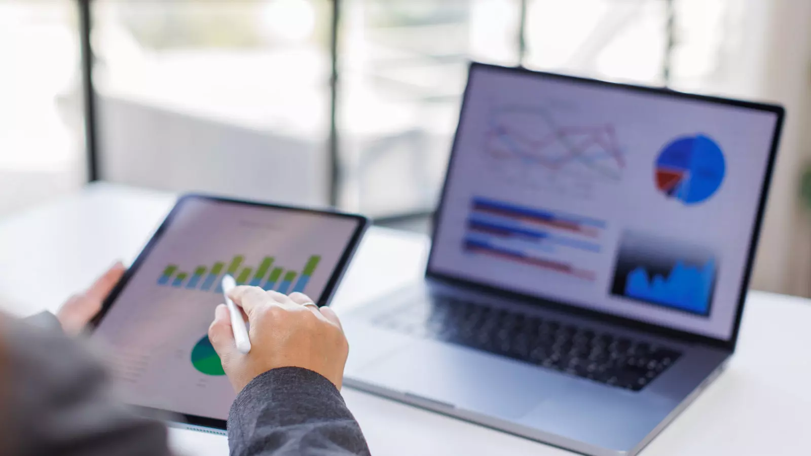 A user interface reviewing complex sales forecasting analysis graphs and market statistical indicators displayed on laptop and tablet screens.