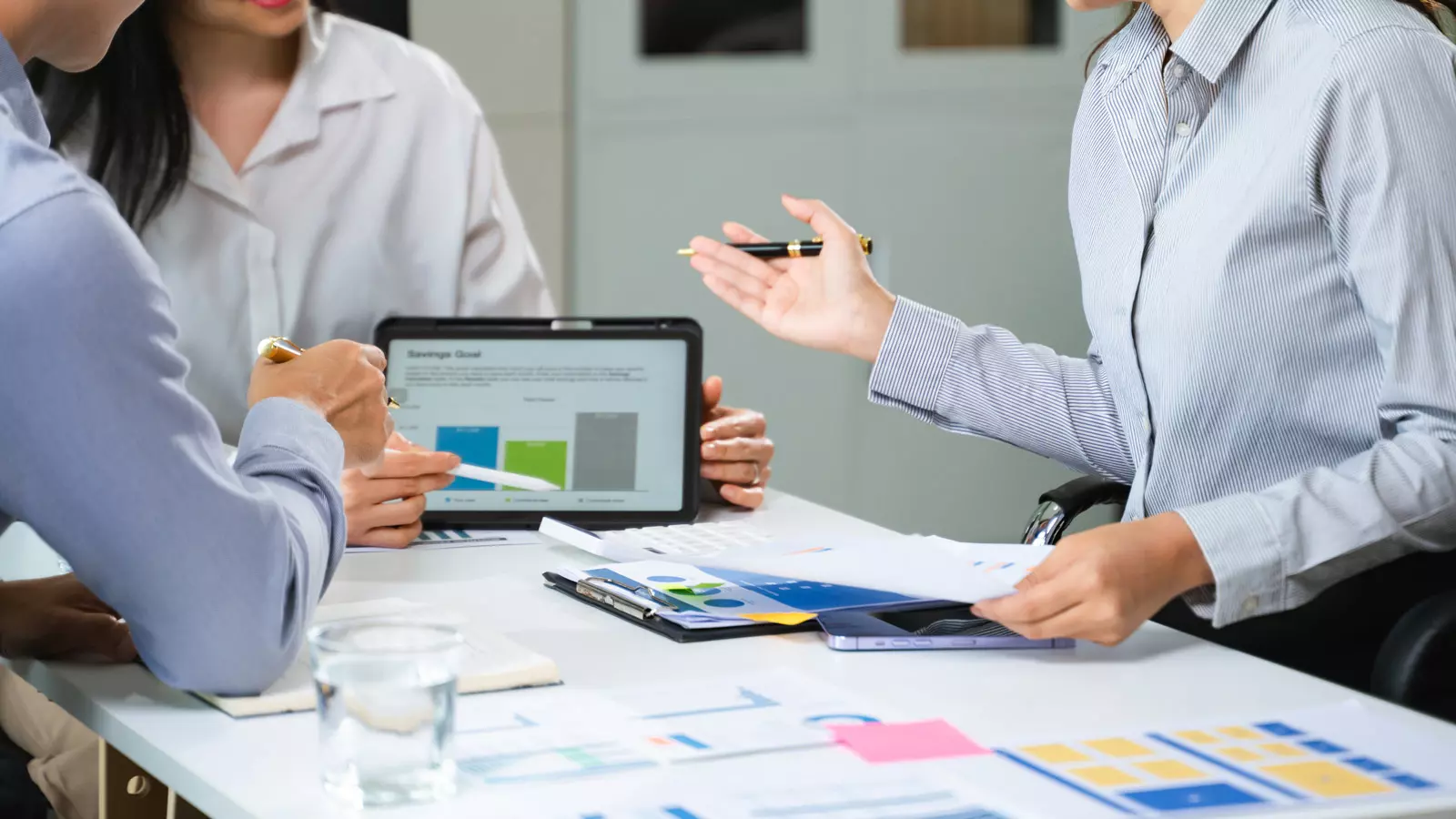 Professionals collaborating and discussing efficient sales forecasting strategies while viewing data charts on a tablet during a business meeting.