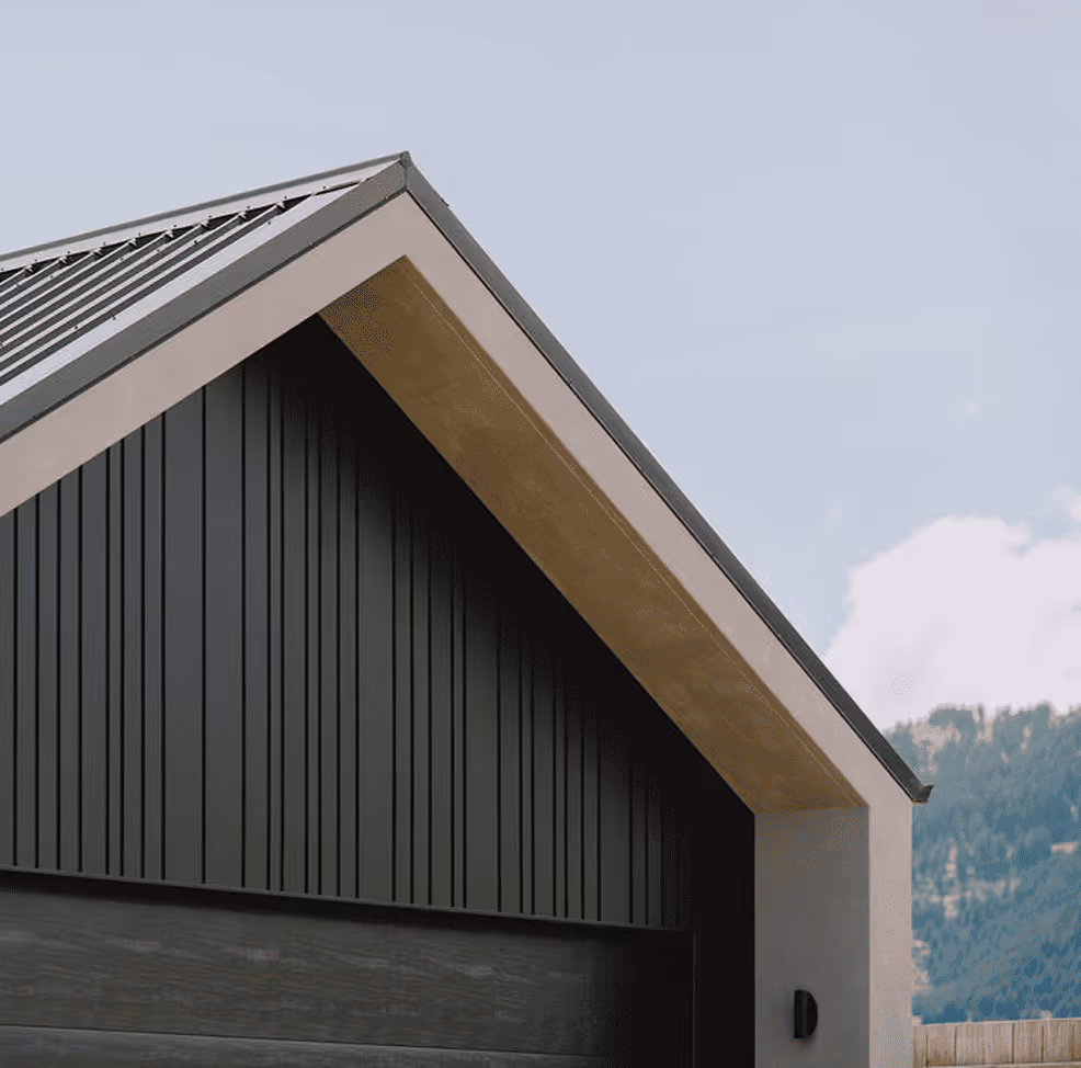Close-up of a modern house roof with dark vertical siding and a light wood underside under a partly cloudy sky.