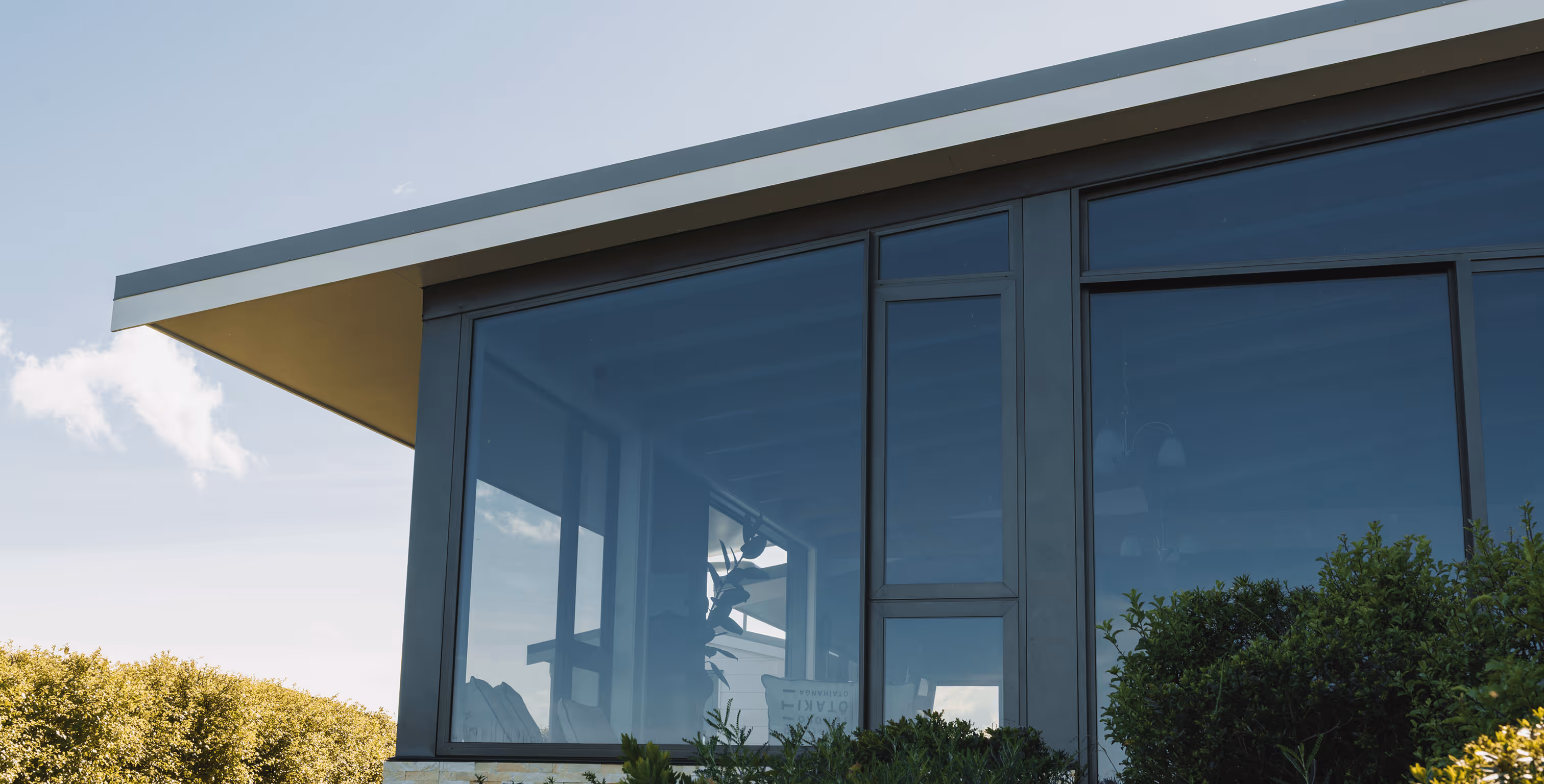 Modern building with large reflective glass windows surrounded by green bushes under a clear sky.