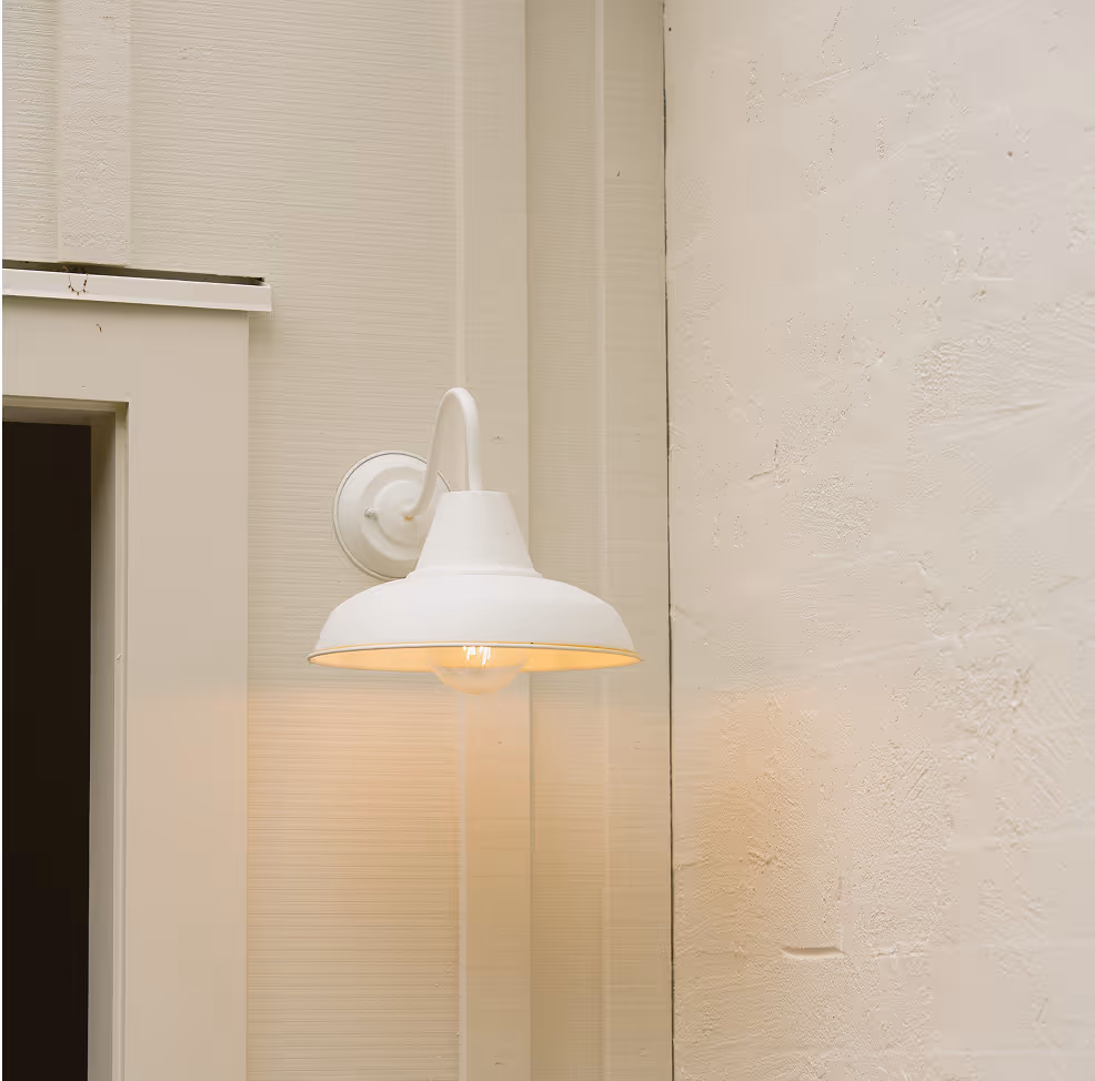White wall-mounted outdoor light fixture illuminated on beige building wall near door frame.