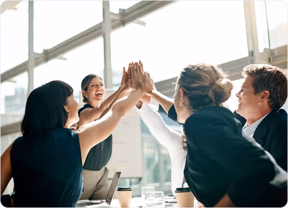 Group of five businesspeople in an office giving a high-five above a table with coffee cups.