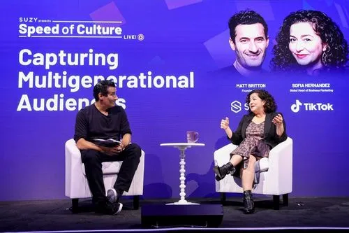 Two people seated on stage having a discussion during SUZY's Speed of Culture event titled 'Capturing Multigenerational Audiences' with portraits and names of Matt Britton and Sofia Hernandez on a purple backdrop.