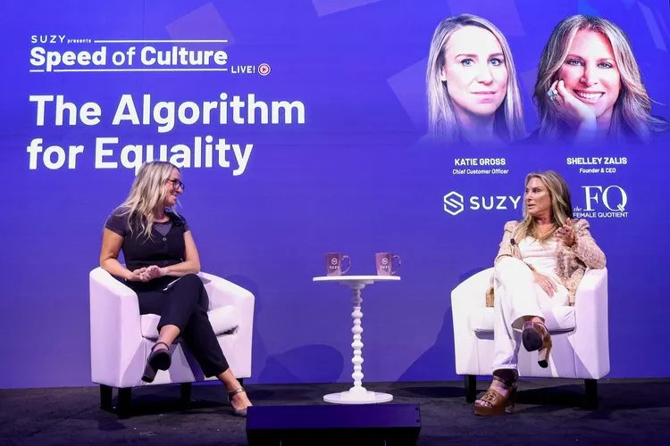 Two women seated on white chairs on a stage during a live event titled 'The Algorithm for Equality' by SUZY Speed of Culture, with portraits and names of Katie Gross and Shelley Zalis displayed on a purple backdrop.