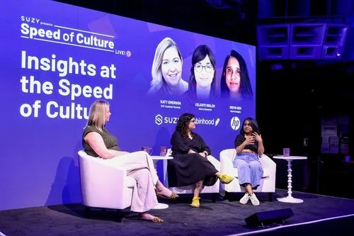 Three women seated on stage chairs having a panel discussion with a large purple backdrop reading 'Suzy presents Speed of Culture Live! Insights at the Speed of Culture' and headshots of Katy Emmerson, Celeste Prullen, and Reetya Sen.