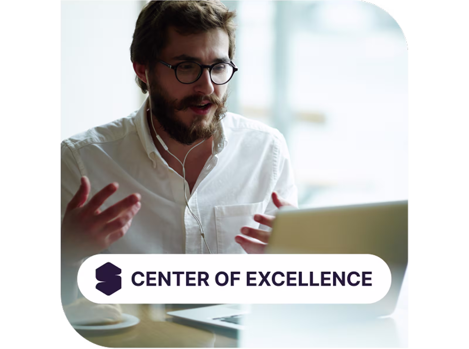Man with glasses and beard speaking on a video call at his laptop, wearing earphones, with “Center of Excellence” text and logo overlay, representing professional virtual collaboration and business expertise.