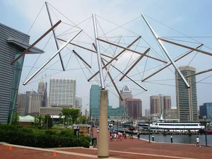 Tensegrity sculpture of steel tubes and cables against a waterfront skyline