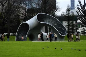 Curved metal pavilion on a lawn with visitors gathered beneath it