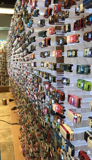 Wall assembled from hundreds of toy cars arranged in rows on shelves