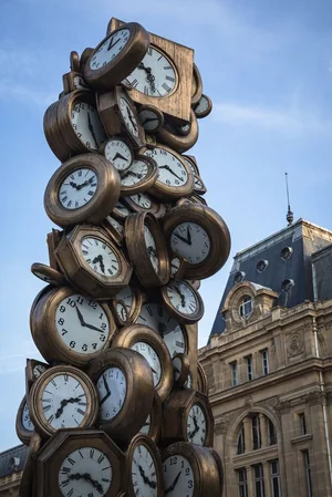 Sculpture stacking dozens of bronze clock faces against a city building