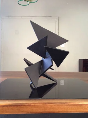 Angular sculpture of black triangular plates balanced on a table