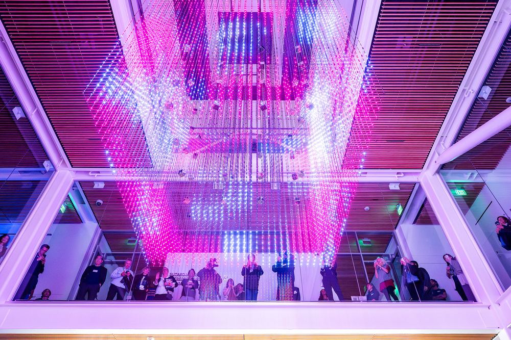 he Strauch Hypercube lit magenta and pink, seen from the floor of the atrium