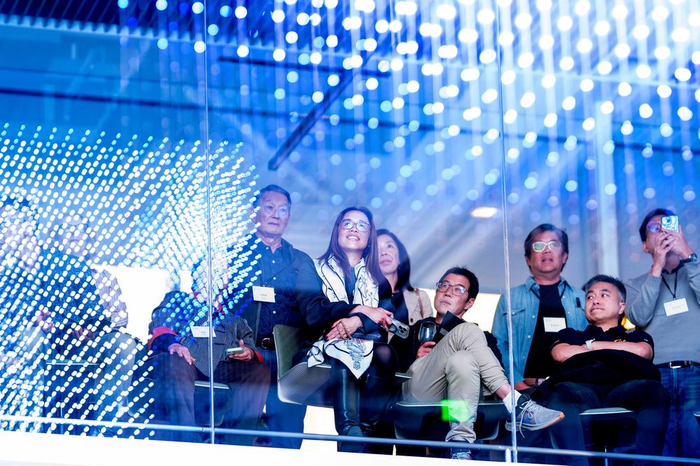 Visitors watching the blue-lit Strauch Hypercube through the atrium glazing