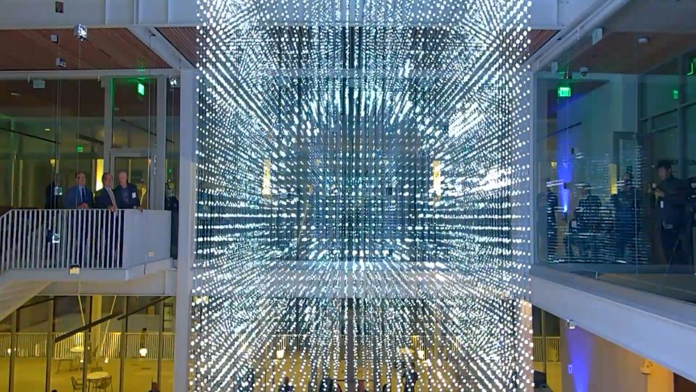 he Strauch Hypercube filling the atrium in white light, visitors on the balcony above