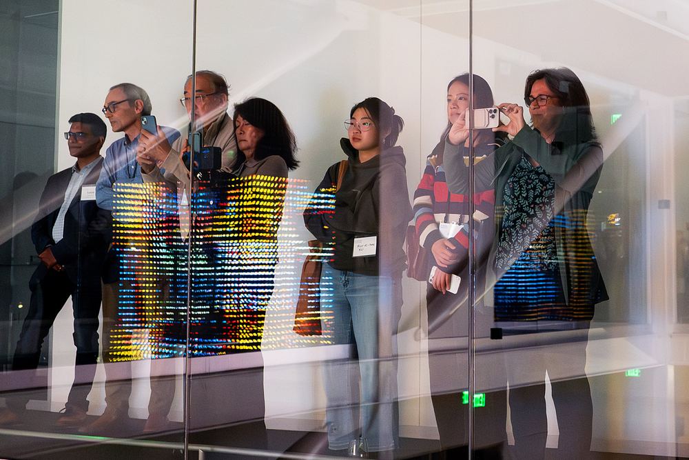 Visitors behind glass watching a multicoloured pattern move through the Hypercube